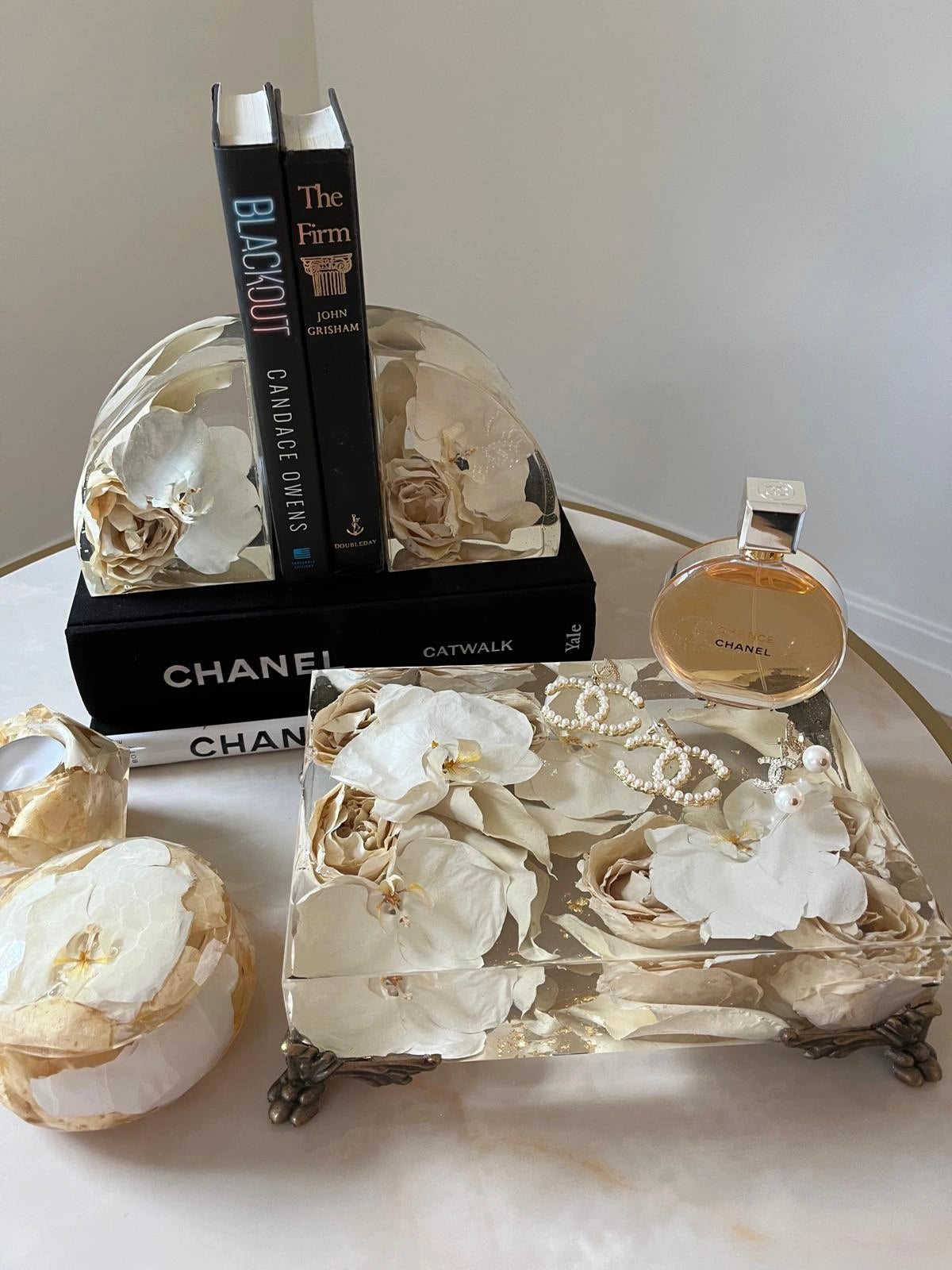 Decorative box with floral design, Chanel books, and a Chanel perfume bottle on a marble surface.