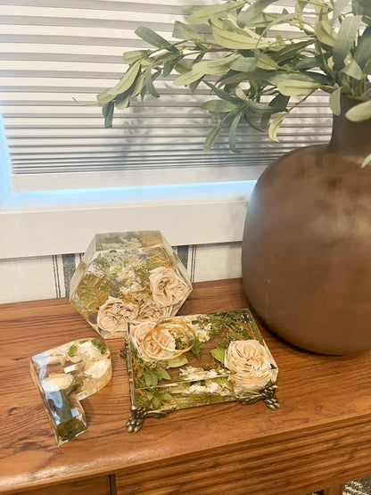 Decorative boxes with pressed flowers on a wooden surface with a plant in the background.